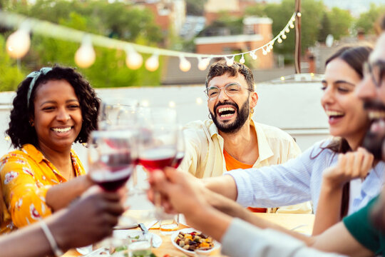Group of diverse friends enjoying a vibrant summer gathering on a city terrace, laughing and clinking wine glasses in a joyful celebration of friendship and shared moments