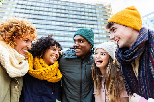 Group of happy multiracial young friends having fun together outdoor in winter. Millennial generation people laughing while hugging each other spending time together. Youth and friendship concept