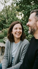 Fototapeta premium Couple laughing together on wooden park bench surrounded by green trees and grass