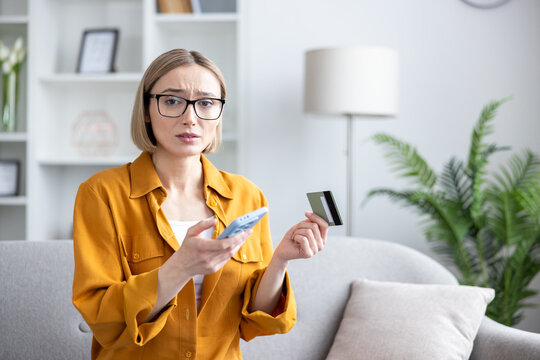 Worried woman at home holding credit card and smartphone, facing online payment failure or scam, stressed about fraud, identity theft and unexpected digital transaction error