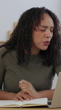 Vertical HD video of young African American woman working on laptop at kitchen table with notebook. Smiling professional female taking notes while working remotely from home talking on video call