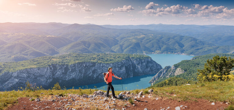 Hiker with backpack and trekking poles standing on a viewpoint, enjoying a panoramic view of the Danube Iron Gates river canyon in Djerdap park