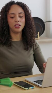 Vertical HD video of young woman suffering from heat while using laptop at home. Young Brazilian female cooling herself with hand fan during remote work, trying to stay comfortable during remote work
