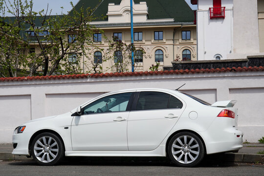 Bucharest, Romania &ndash; April 13, 2026:  Closeup side view of Mitsubishi Lancer white car parked on street in front of historic building