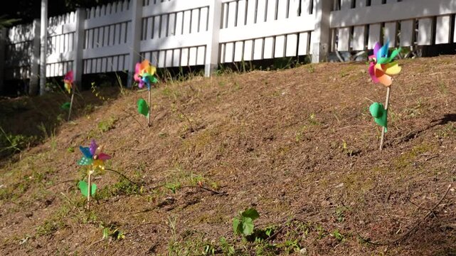 Windmills against a fence. Multicolored toy windmills spinning in the wind. Bright multicolored plastic toy windmills next to a white wooden fence in the sun.