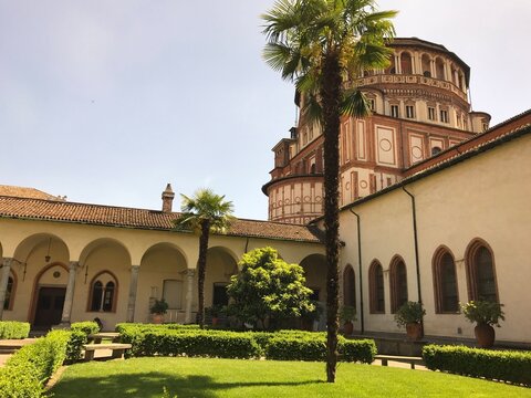 Church apse rising above the cloister garden in Milan in Santa Maria delle Grazie, Milan, Italy. The image presents architecture, heritage, and tourism in a clear, factual travel photograph.