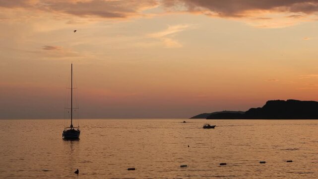 progressive sunset over the sea with boats and distant landforms in a wide-angle shot, peaceful and serene ocean view for travel and nature relaxation content. orange and pink hues.