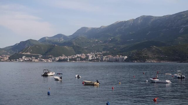 The tranquil coastal town of Budva, with boats and buildings by the water, surrounded by rocky terrain and mountains, offers a peaceful view of nature and a place to relax.