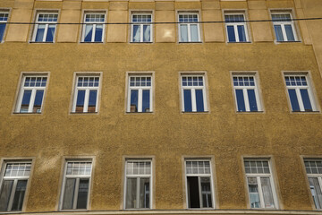 Obraz premium Textured yellow facade in Vienna with rows of white-framed windows and strong geometric repetition, offering an authentic European architectural backdrop for travel, editorial, and design projects.