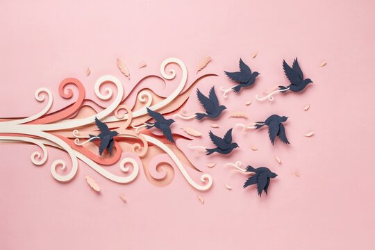 Paper cut art of flock of birds flying with ornamental wind swirls on pastel pink background