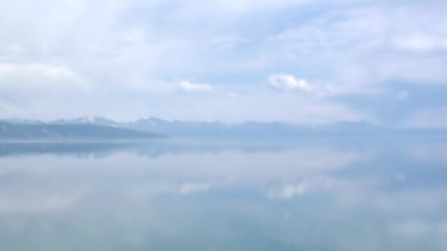 Experience the tranquil majesty of Mountain Lake Khuvsgul in Mongolia. Its crystal waters create a perfect reflection of the immense, cloudy sky and distant, snow-kissed mountain range.