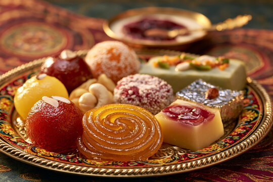 Close-up of colorful Indian sweets including gulab jamun, jalebi, and barfi arranged on ornate tray, festive dessert