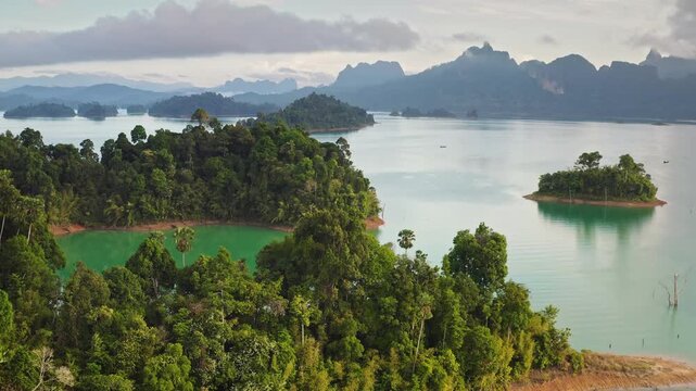 KHAO SOK National Park, tropical rainforest islands floating on Cheow Lan Lake, surrounded by towering karst limestone mountains under a cloudy sky. Thailand famous travel destination. Aerial panorama