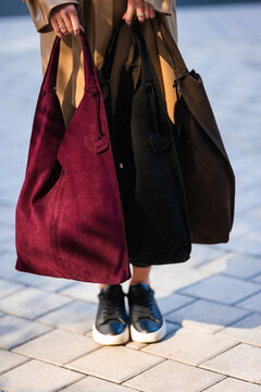 Stylish woman carrying suede tote bags in burgundy, black and brown with heart charms, beige trench coat and layered streetwear on urban pavement fashion scene, with bag, bags, tote, suede detail