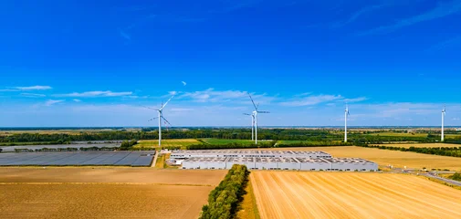 Fotobehang Kasteel Wind turbines and solar panels in a rural landscape during the day. Wind turbines are turning above fields of crops and solar panels. A clear sky shows no clouds.  © Vadim