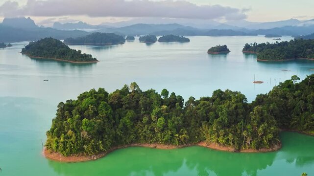 Cheow Lan Lake showing numerous karstic limestone islands covered in lush green rainforest, surrounded by stunning turquoise and emerald water in Khao Sok National Park, Thailand. Drone flight shot
