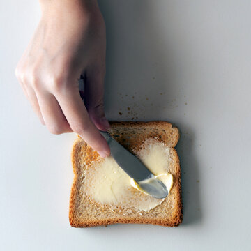 Hand spreading butter on toasted bread with a knife, simple breakfast preparation, everyday home cooking and comfort food concept with copy space