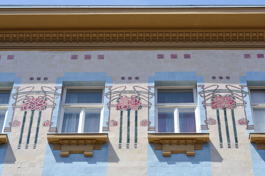 A colorful Art Nouveau tiled building facade from 1904 features geometric patterns and detailed red rose mosaics between rectangular windows