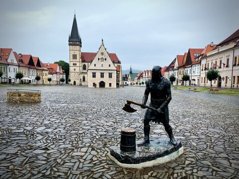 Bronze executioner statue in Town Hall Square in Bardejov, Slovakia. Historic UNESCO heritage plaza featuring cobblestone pavement, Old Town Hall, St. Giles Basilica, and colorful burgher houses.