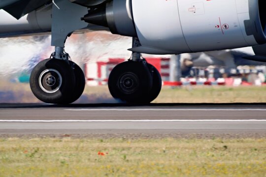 The landing gear of an aircraft touches down on the runway, with the wheels visible and smoke trails from braking. The scene captures the moment of landing during a flight.