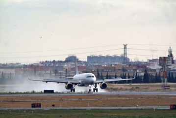 Fototapeta premium Airplane landing on airport runway with jet engine exhaust and city skyline in distance