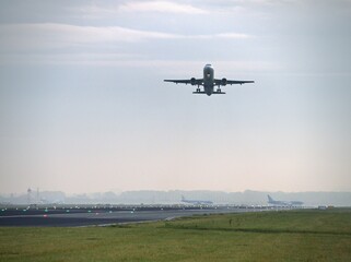 Fototapeta premium Airplane taking off from airport runway at sunrise with distant planes parked on the tarmac