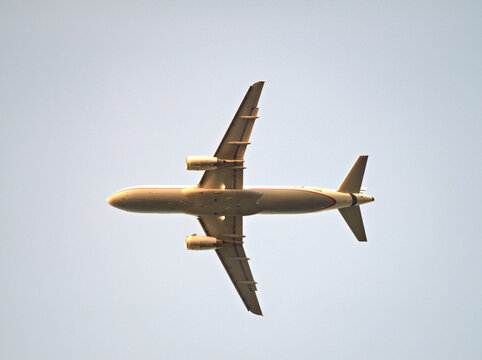 A passenger jet aircraft in flight against a clear blue sky, viewed from below.