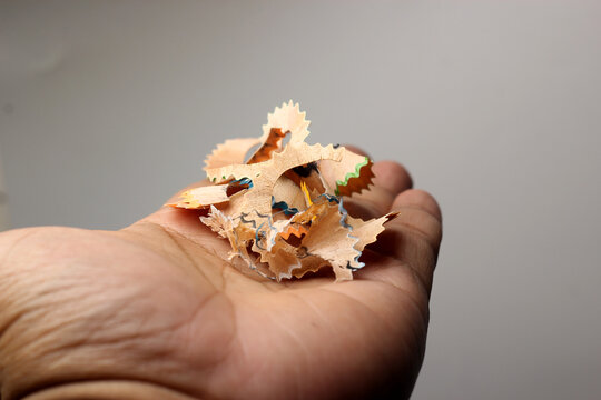 A person holding a small cluster of colorful, curled pencil shavings in the palm of an open hand