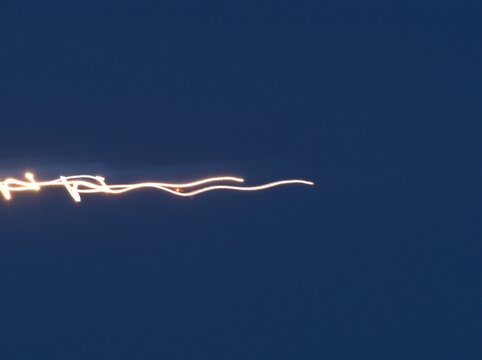 Abstract light trail streak showing motion blur with glowing orange lines moving horizontally across a dark blue sky