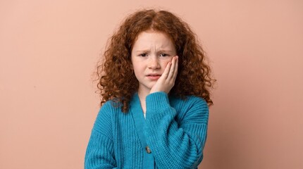 Fototapeta premium Redhead girl suffering from toothache and dental pain, young child with curly hair holding cheek in discomfort, pediatric healthcare and oral hygiene concept