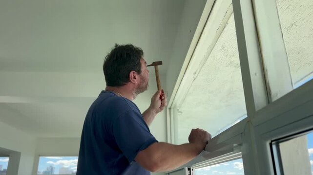 Handyman using a hammer while working on a window frame during a home repair and installation project.