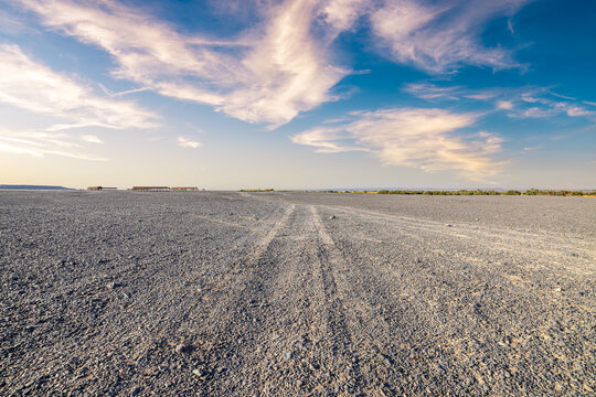 Desert sand track leading through a vast gravel plain under a blue sky with wispy clouds in Xinjiang, China