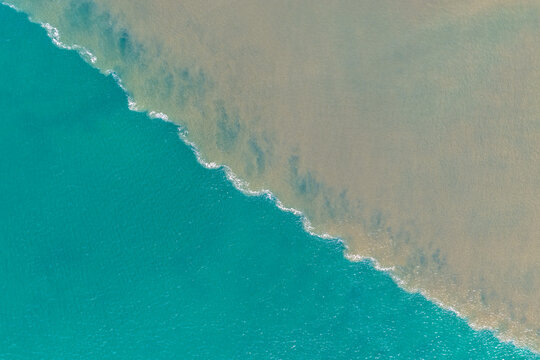 Aerial downward view of brown floodwaters flowing into the ocean and meeting clear turquoise seawater, creating a striking boundary of contrasting colours, sediment and swirling water patterns 