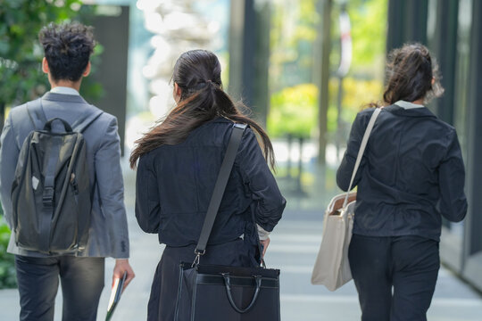 A young Asian and Latina business team walking off together after an outdoor meeting through a modern arcade planted with greenery, a modern picture of teamwork in a green city district