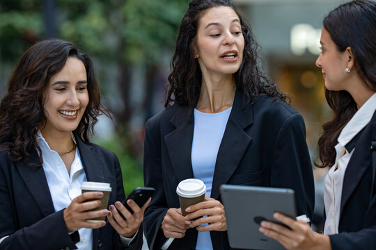 A team of three Hispanic businesswomen in matching dark suits, absorbed in the numbers on screen, hold an impromptu walking meeting over a tablet, a female leadership theme.