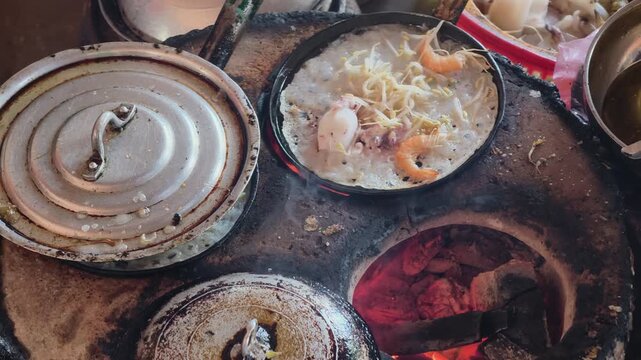 Cooking process of traditional Central Vietnamese style mini seafood pancakes, vendor lifting cooked pan off charcoal stove