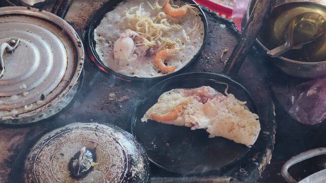 Traditional Central Vietnamese mini pancakes (Banh Xeo) being cooked on multiple small charcoal stoves with lids and fresh seafood , 60fps