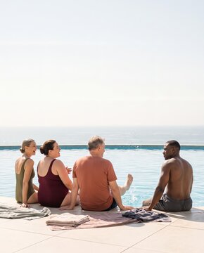 Friends sitting at the edge of an outdoor pool with their feet in the water