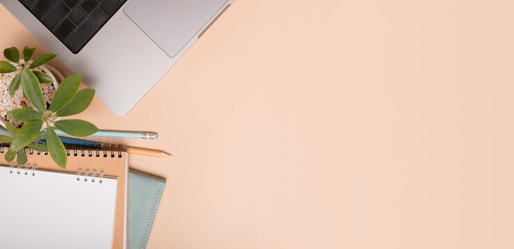 Workspace setup with laptop, notebook, plant, and stationery on beige surface. Banner format