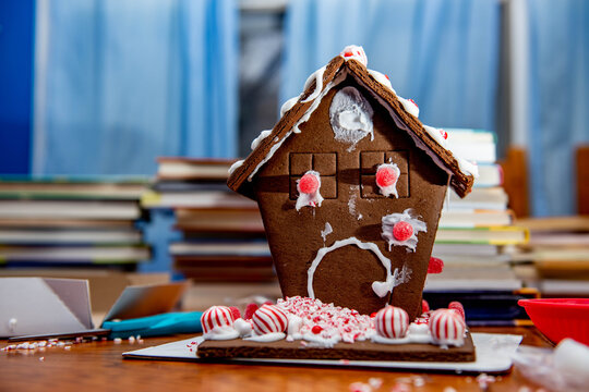 A messy homemade gingerbread house wood table trimmed with peppermint candy and dripping icing, a perfect Christmas baking fail example. 