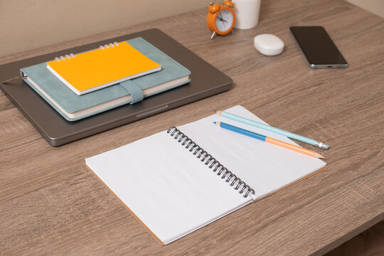 Desk setup with notebooks, clock, and phone during daytime