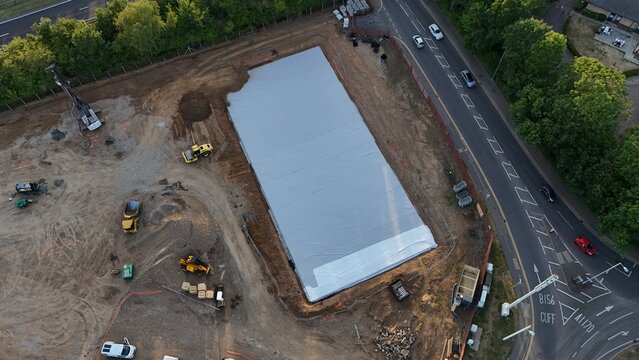 Aerial view of construction site for a new supermarket car park featuring a large concrete foundation, heavy machinery, and surrounding roads in Cheshunt, England, United Kingdom.