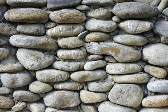 A rustic stone wall featuring stacked river rocks and cement, symbolizing strength, durability, and natural architecture.