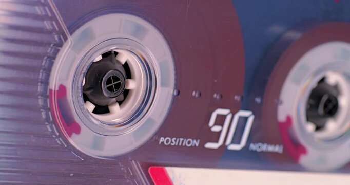 Spinning Cassette Reel Close-Up. Macro view of magnetic tape reel rotating inside a transparent audio cassette with shallow focus.