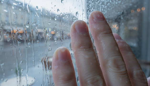 Hand Touching Rain-Streaked Window with City View