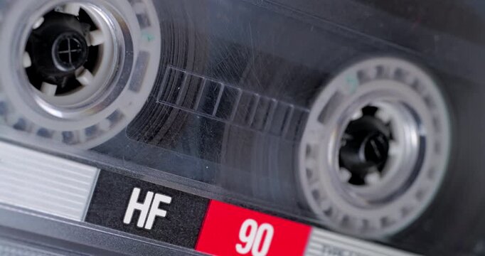 Spinning Cassette Reel Close-Up. Macro view of magnetic tape reel rotating inside a transparent audio cassette with shallow focus.