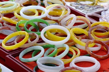 Vibrant collection of colorful jade and stone bangles displayed on a red tray, symbolizing elegance and prosperity. © ProArt Studios