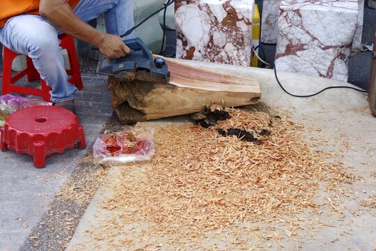 Skilled craftsman using an electric planer on aromatic xa xi wood, creating fragrant shavings for sachets.