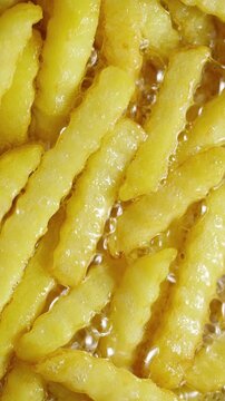 French fries in boiling oil. Macro view of golden potato fries bubbling and sizzling during deep frying.