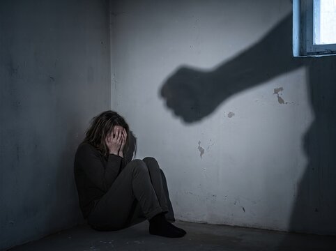 Terrified woman cowering in corner with menacing shadow of raised hand